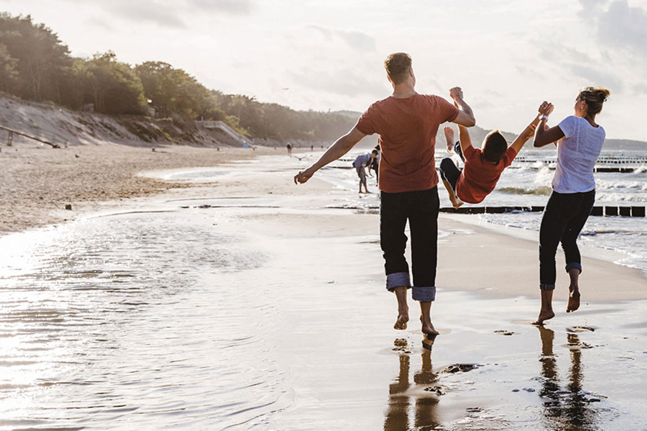 Eine Familie läuft Hand in Hand am Strand entlang, während die Wellen sanft ans Ufer schlagen.