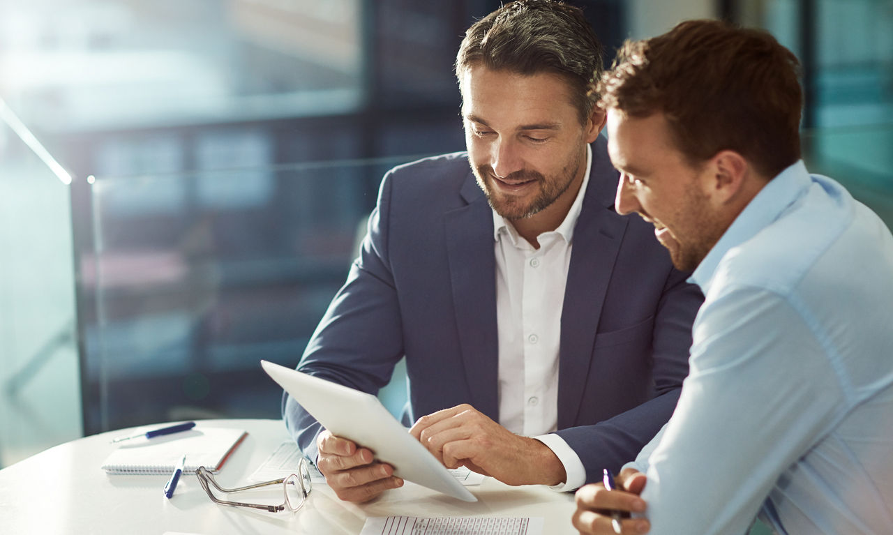 Zwei Business-Männer sitzen gemeinsam an einem Tisch und begutachten ein Blatt Papier