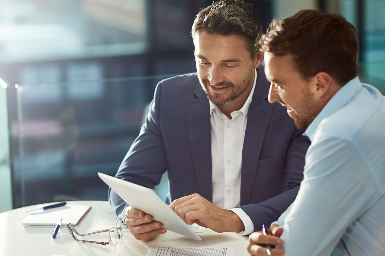 Zwei Business-Männer sitzen gemeinsam an einem Tisch und begutachten ein Blatt Papier