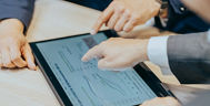 Hände die auf ein Tablet zeigen.