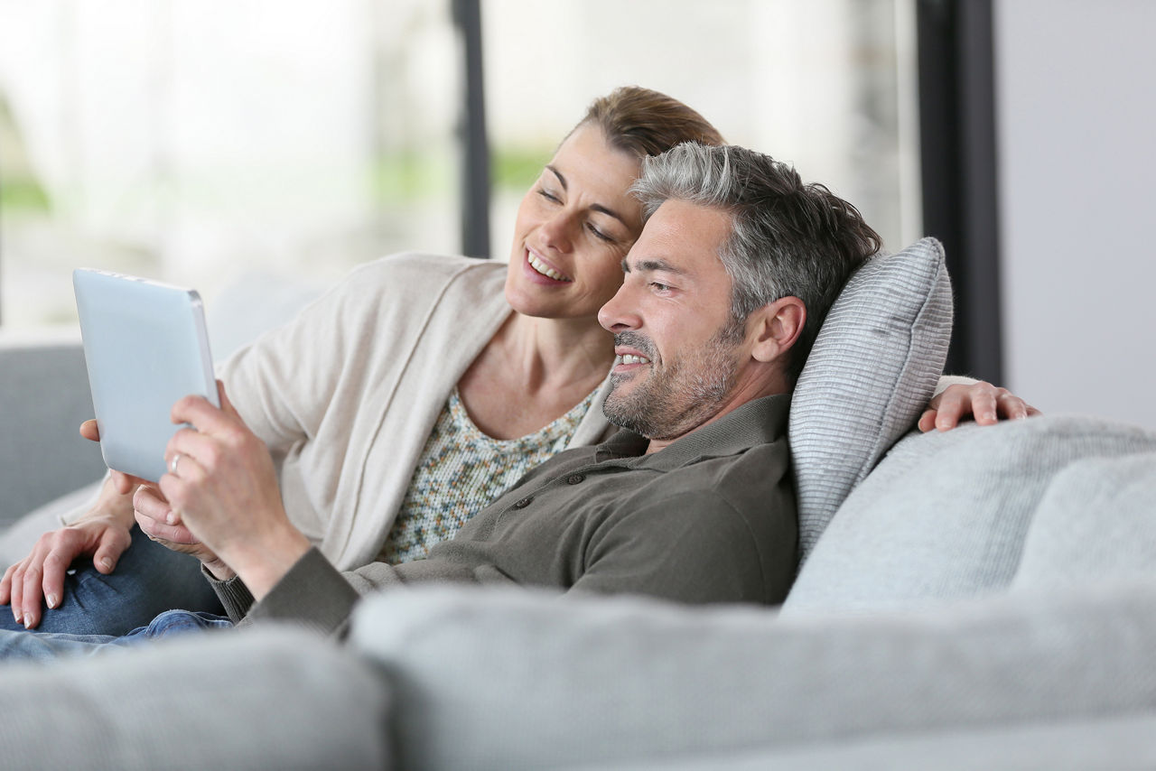 Glückliches Ehepaar mit Tabelt auf dem Sofa