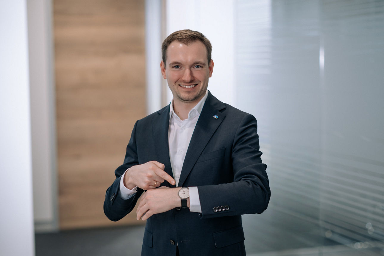 Lächelnder Mann im Anzug, der mit der Hand auf seine Armbanduhr zeigt