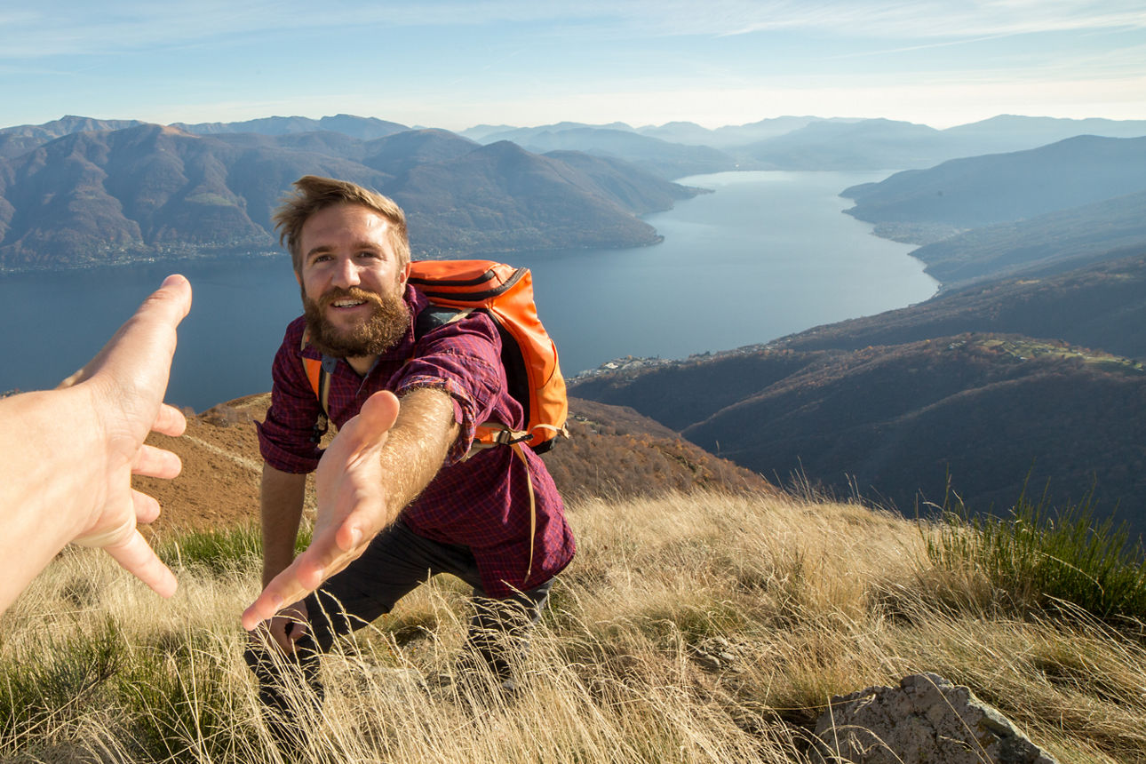 Ein Mann auf dem Gipfel eines Berges mit einem See im Hintergrund.