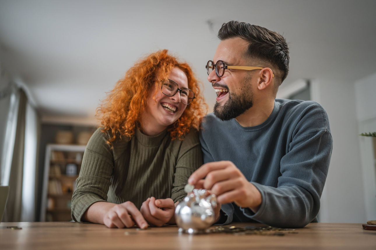 Erwachsenes glückliches Paar spart Geldmünzen im Sparschwein zu Hause