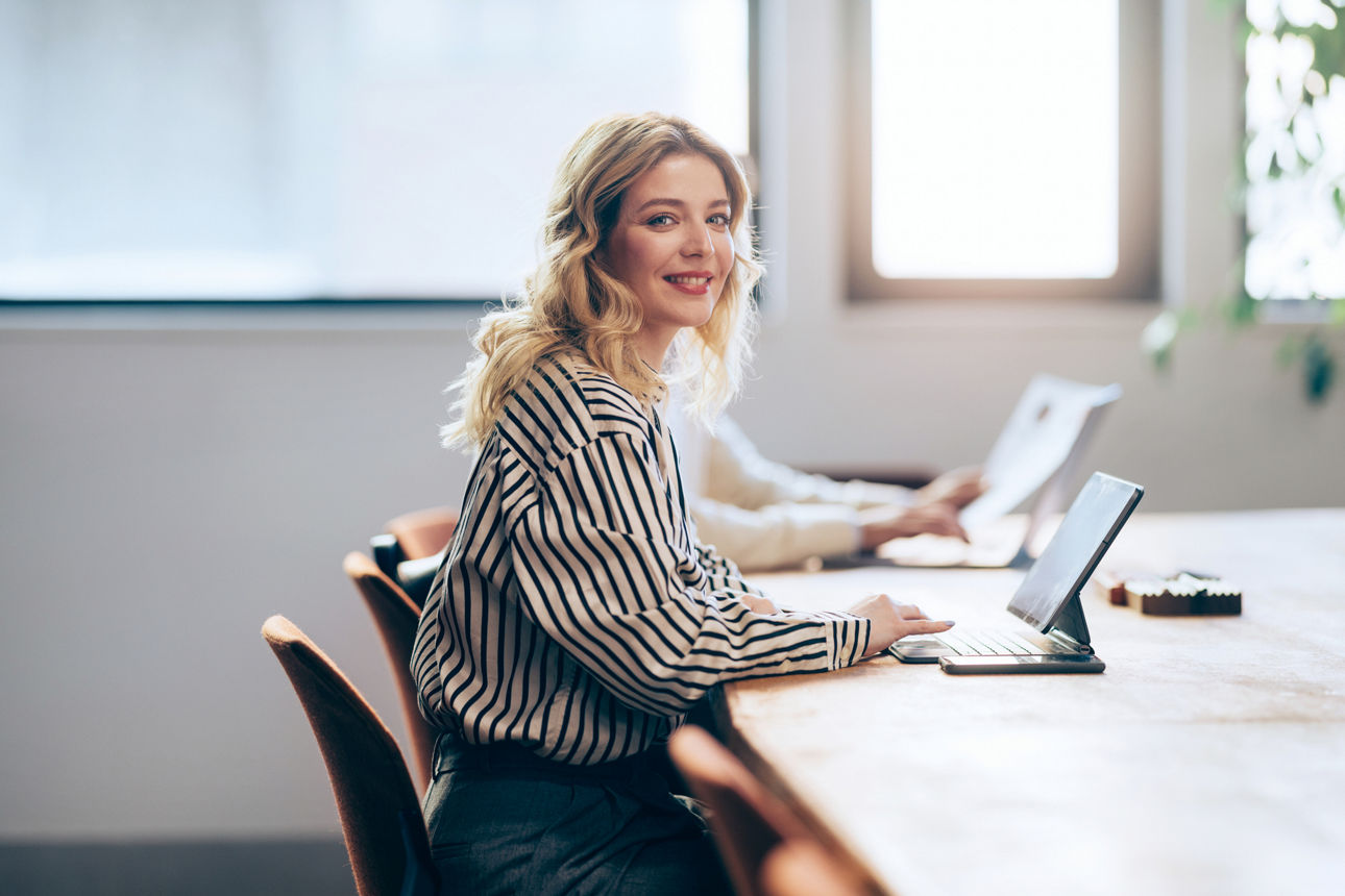 In this office setting, a cheerful professional woman uses her tablet, her smile reflecting the ease and pleasure of her work.