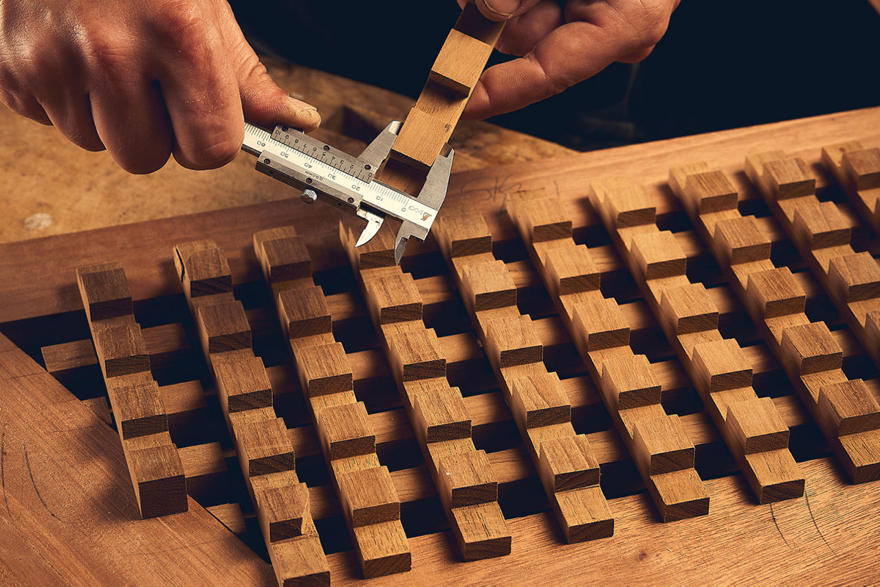 Hände messen präzise ein Holzstück mit einer Schieblehre auf einer Arbeitsfläche mit Holzstruktur