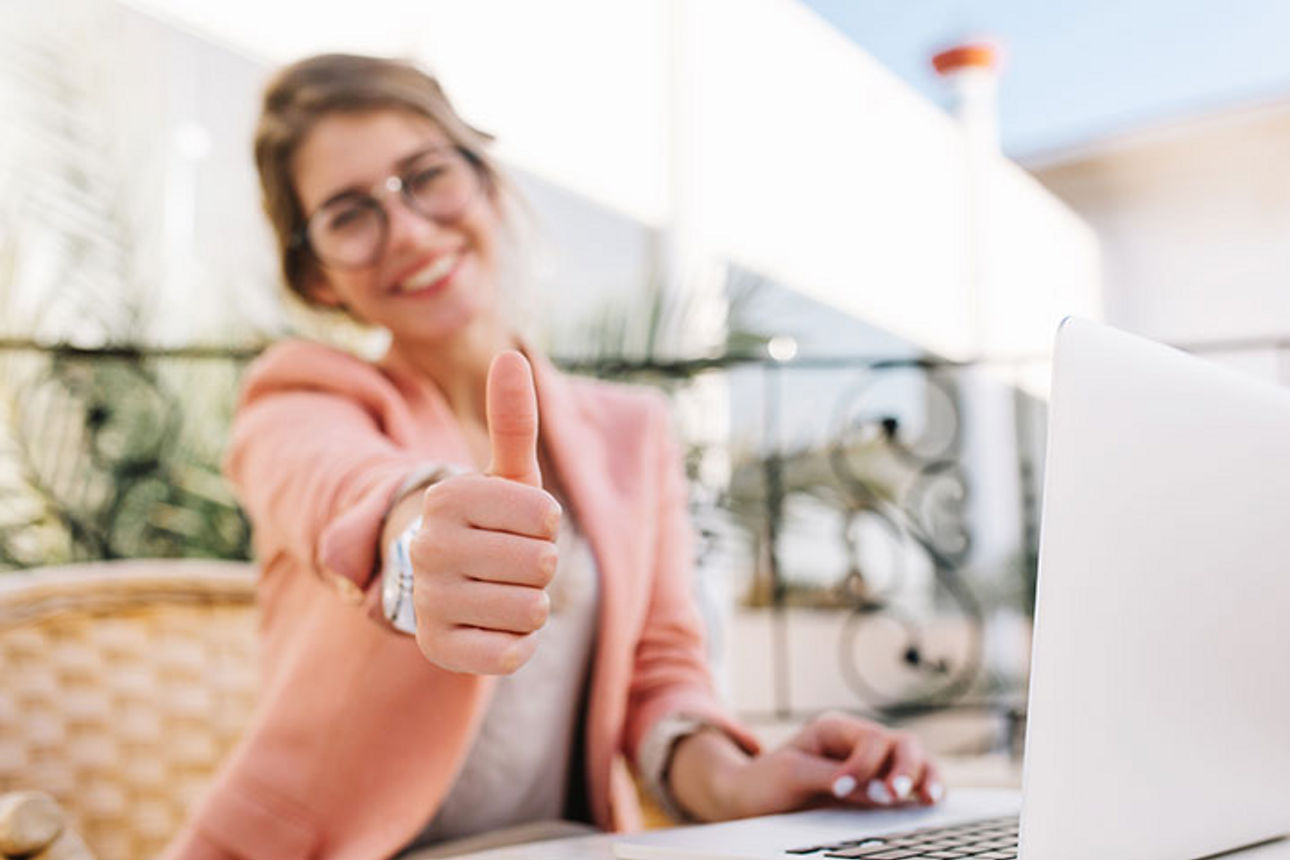 Junge Frau mit Laptop zeigt Daumen nach oben