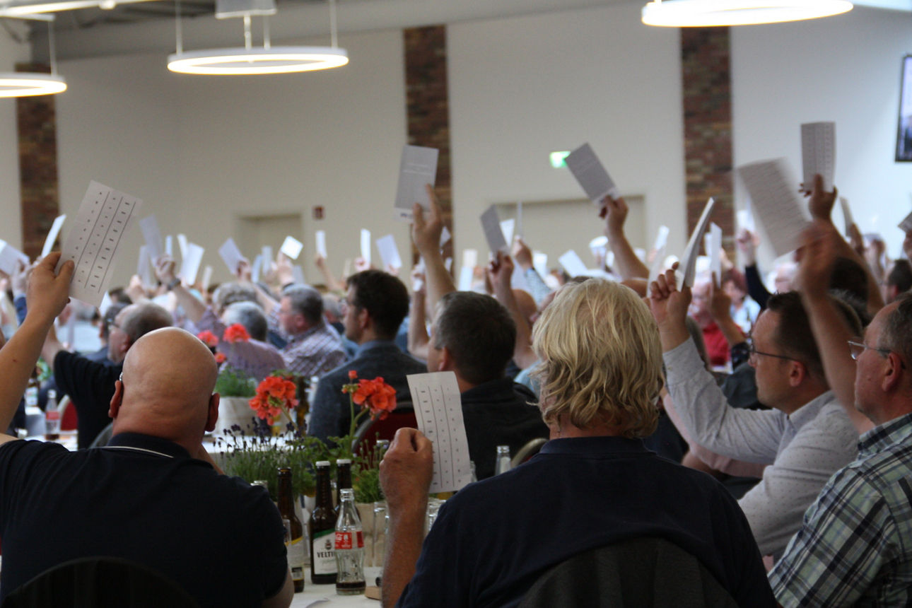 Bild einer Vertreterversammlung, viele Menschen die Stimmkarten heben