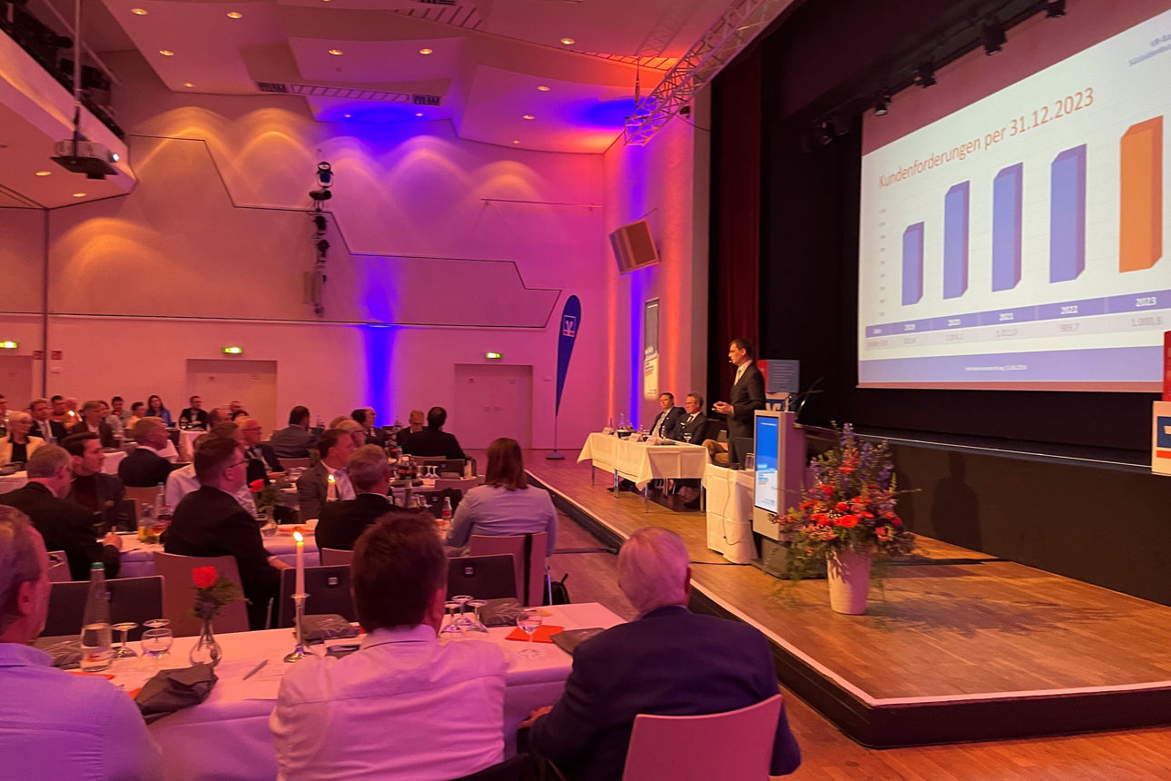 Foto unserer Vertreterversammlung - ist sind Gäste im Vordergrund zu sehen und auf der Bühne stehen die Vorstände der Bank