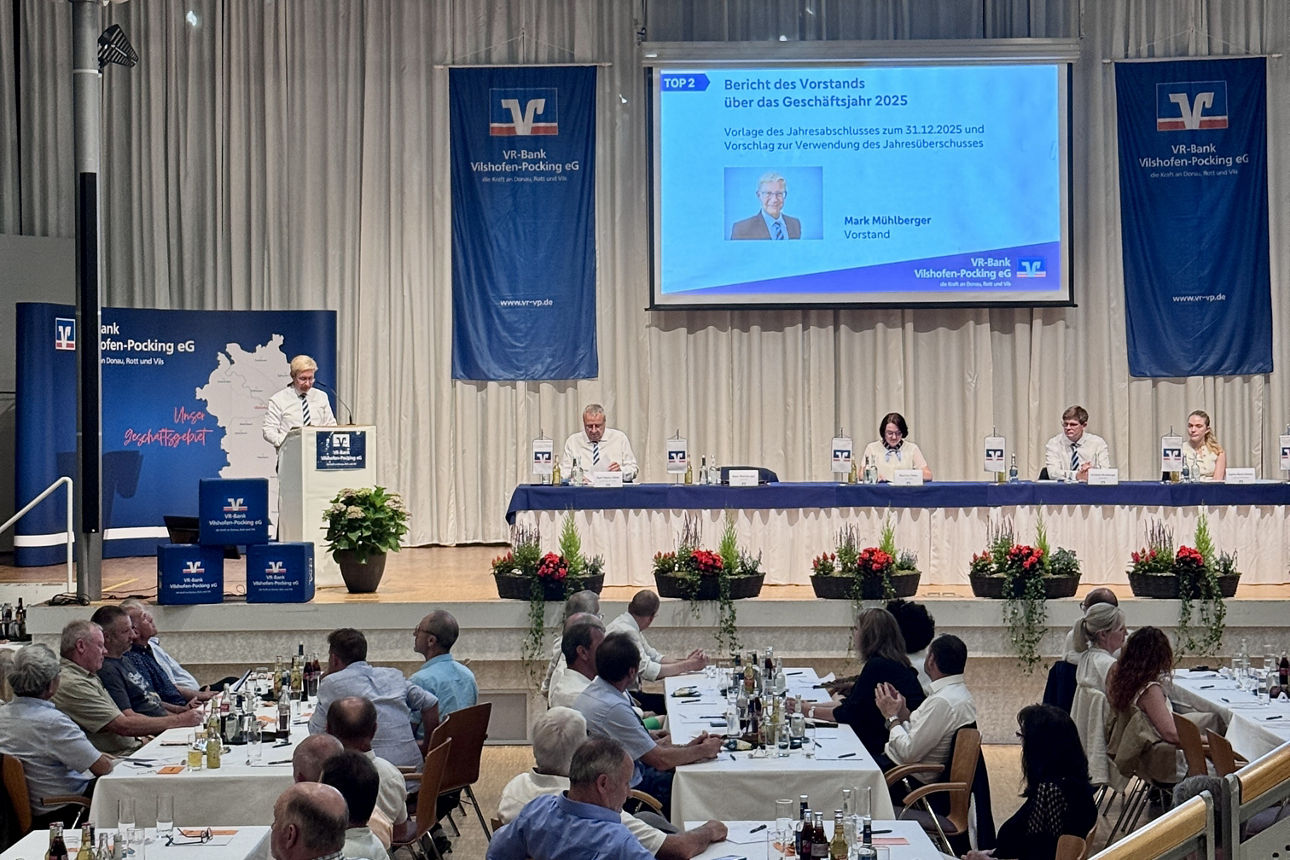 Vertreterversammlung Sprecher am Pult auf Podium mit sitzenden Personen an langem Tisch