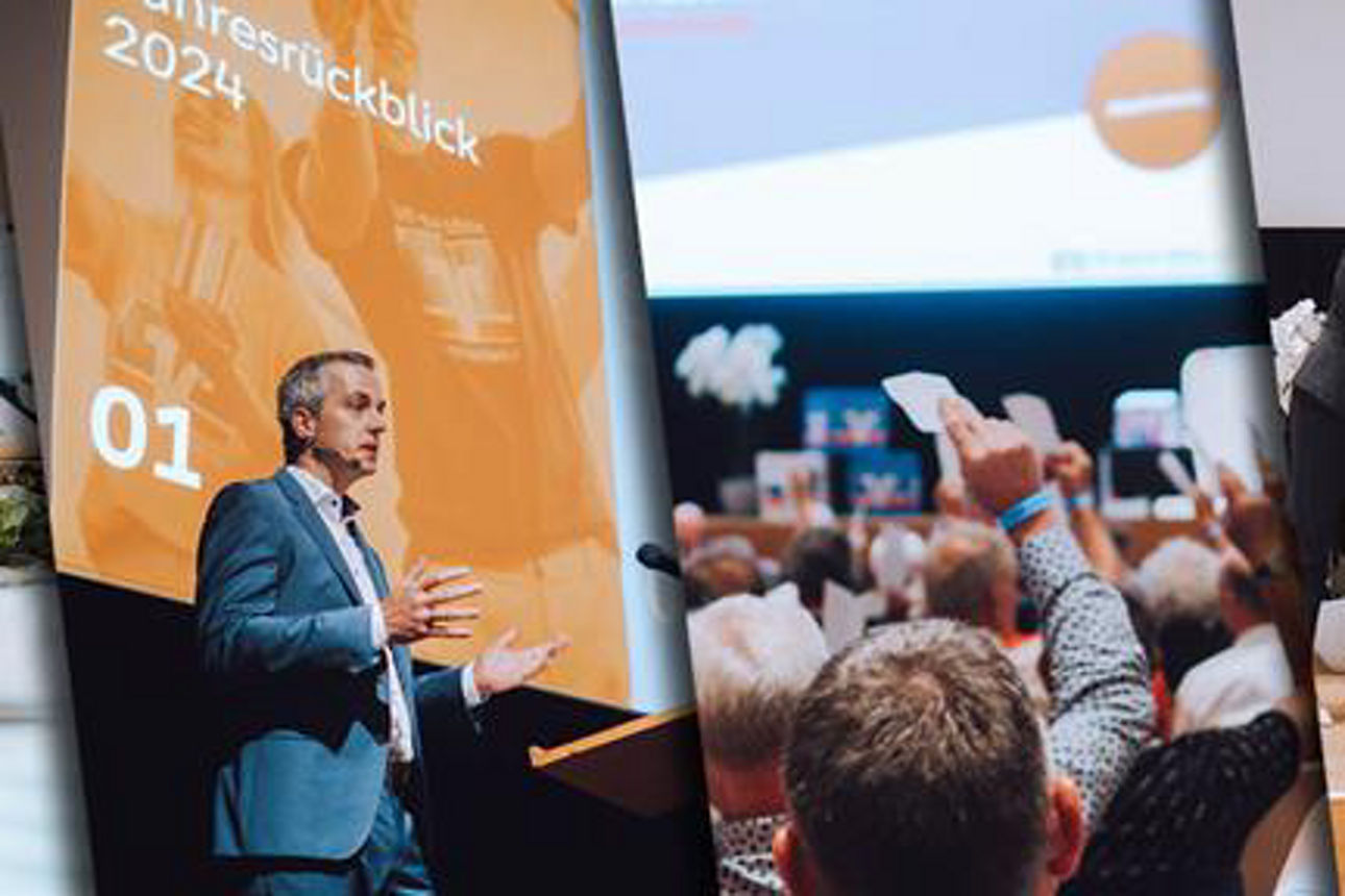 Personen mit Stimmzetteln in der Hand, ein mann am Rednerpult, drei Personen auf der Bühne