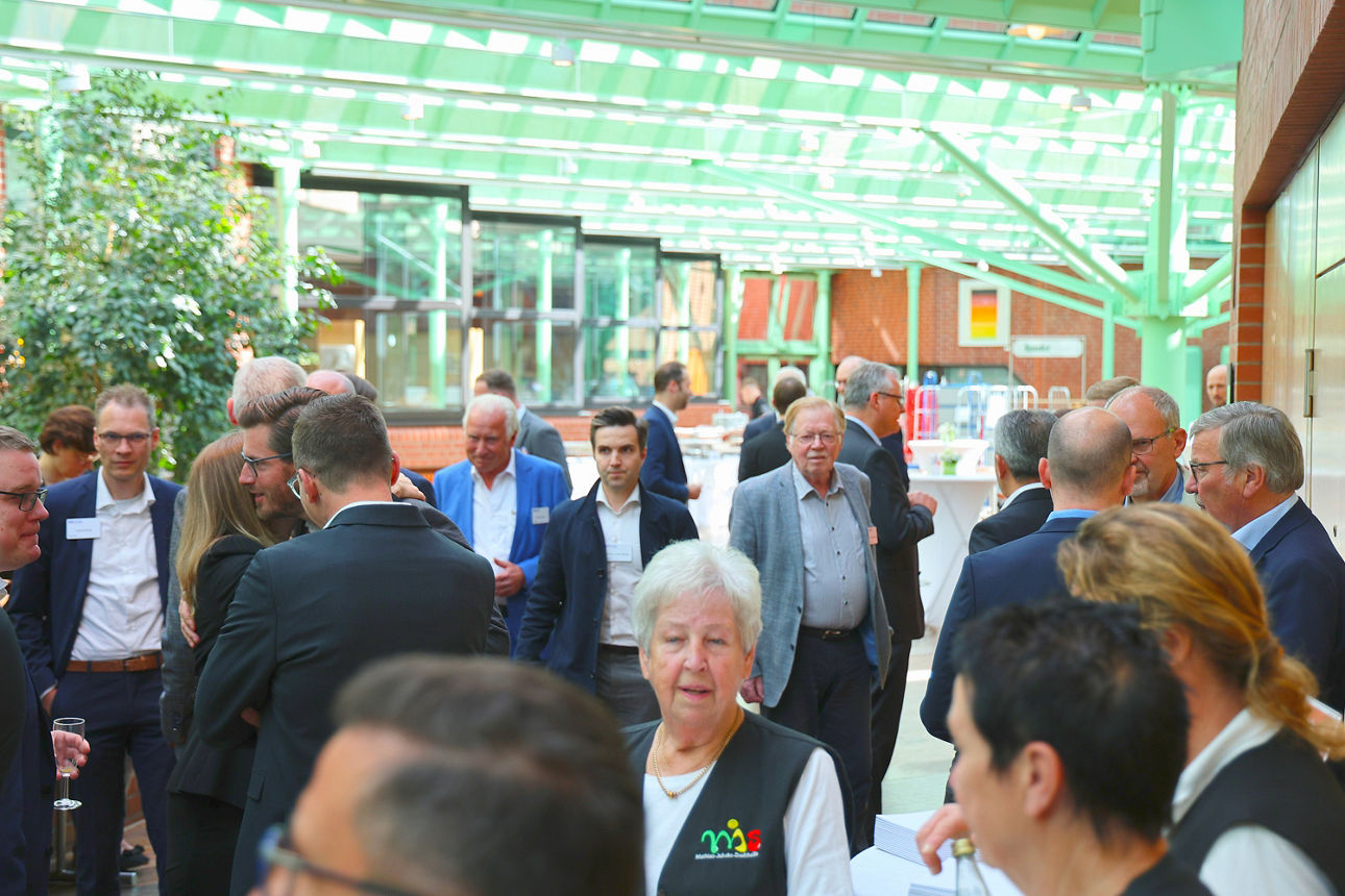 In einem hellen großen Raum mit modernem Glasdach stehen zahleiche Personen, alle tragen ein Namensschild. und die meisten unterhaten sich. Aufgenommen wurde das Bild auf der Verteterversammlung der Volksbank Ruhr Mitte 2025.