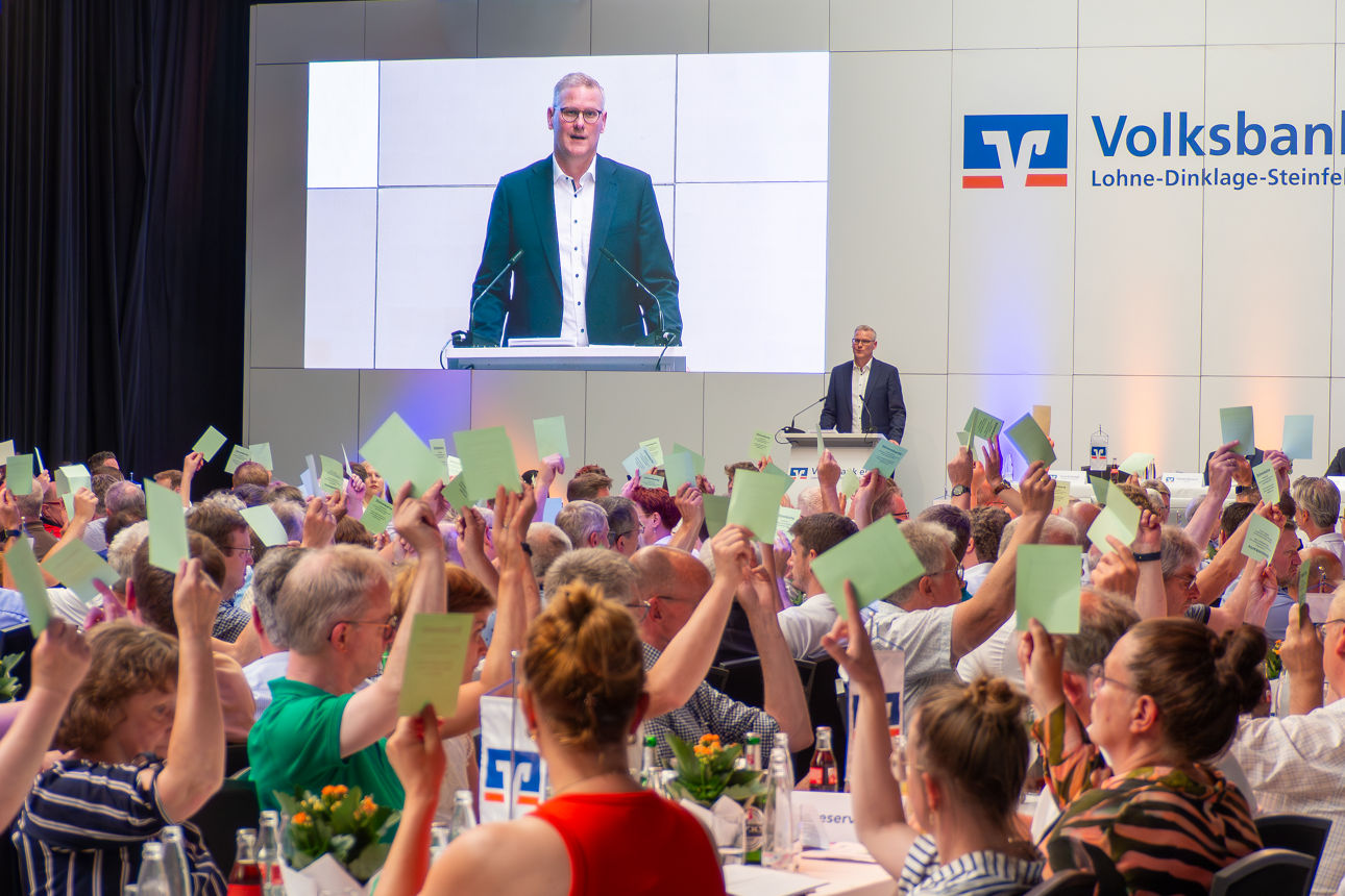 Auf einer Versammlung halten die Besucher einen grünen Stimmzettel hoch.
