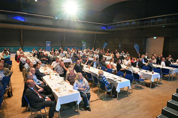 Das Bild zeigt einen großen Konferenzraum, der mit Menschen gefüllt ist.