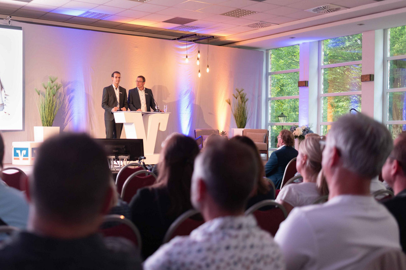 Der Vorstand, Stefan Korte und Norbert Scholtholt, der Volksbank Schermbeck auf einer Bühne an einem Rednerpult