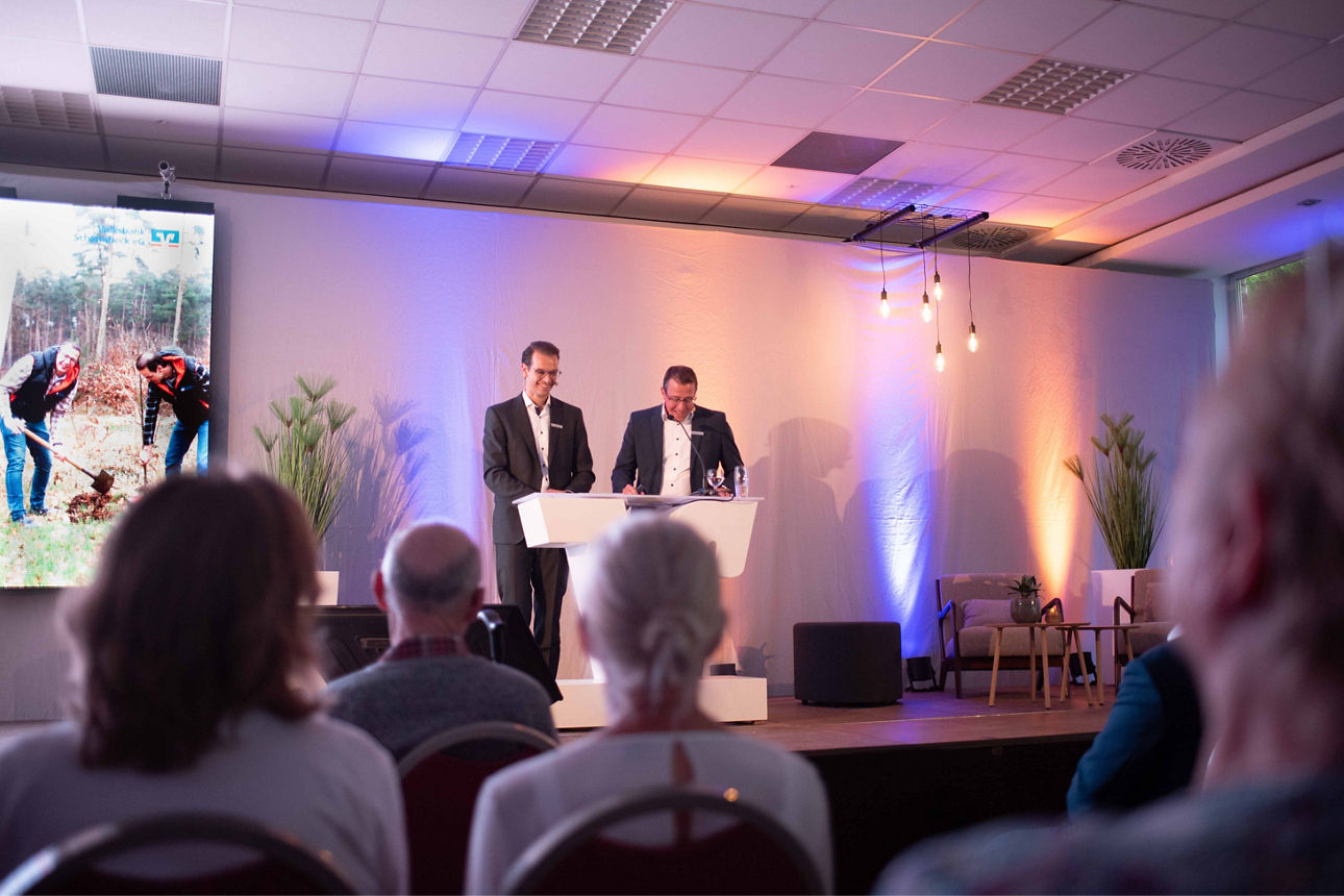 Der Vorstand, Stefan Korte und Norbert Scholtholt, der Volksbank Schermbeck auf einer Bühne an einem Rednerpult