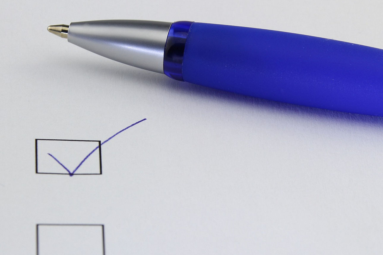 Kugelschreibervorderteil mit herausstehender Miene, und zwei quadratische Kästchen, von denen das erste Angekreuzt ist.