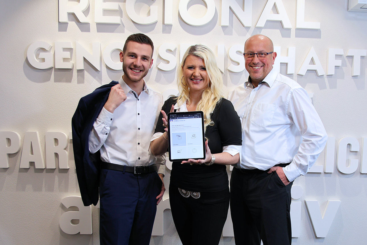 Drei lächelnde Mitarbeitenden halten ein Tablet mit dem geöffneten Wahlportal in die Kamera