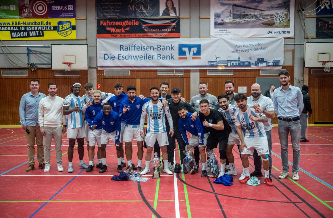 Basketballmannschaft mit Betreuern in Turnhalle, Gruppenfoto vor Sponsorenbanner