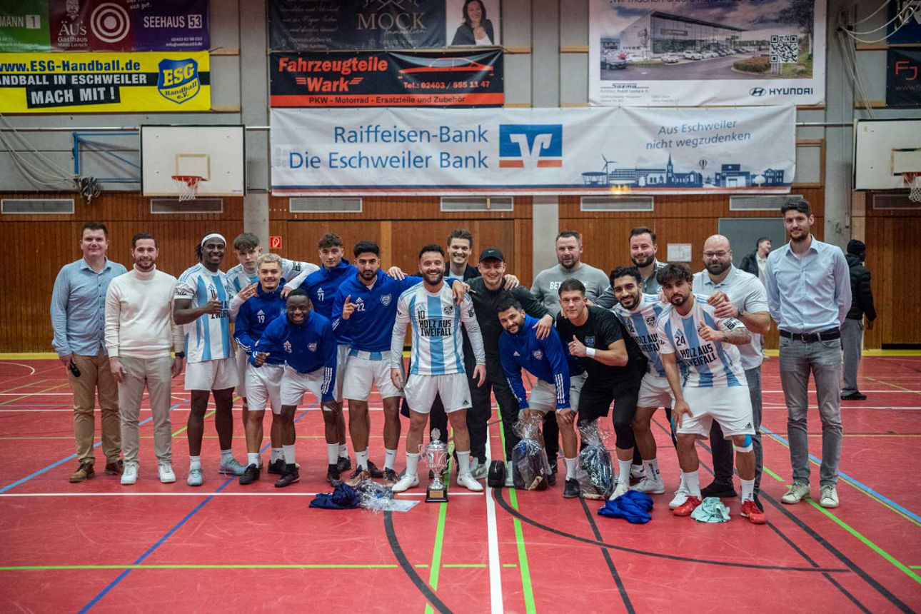 Basketballmannschaft mit Betreuern in Turnhalle, Gruppenfoto vor Sponsorenbanner
