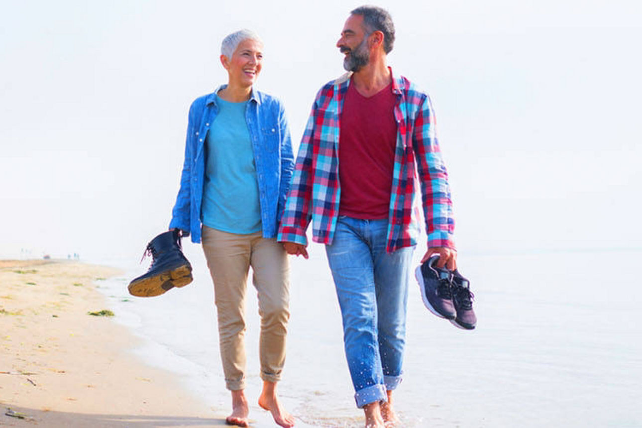 Glückliches älteres Paar geht Hand in Hand am Strand entlang