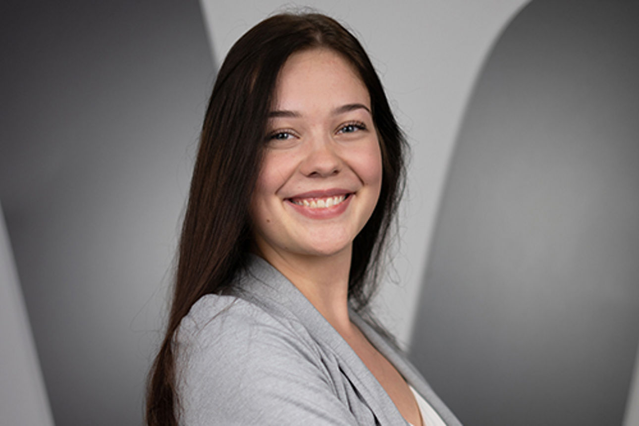 Eine junge Frau steht mit verschränkten Armen vor dem Lodo der Volksbanken-Raiffeisenbanken.