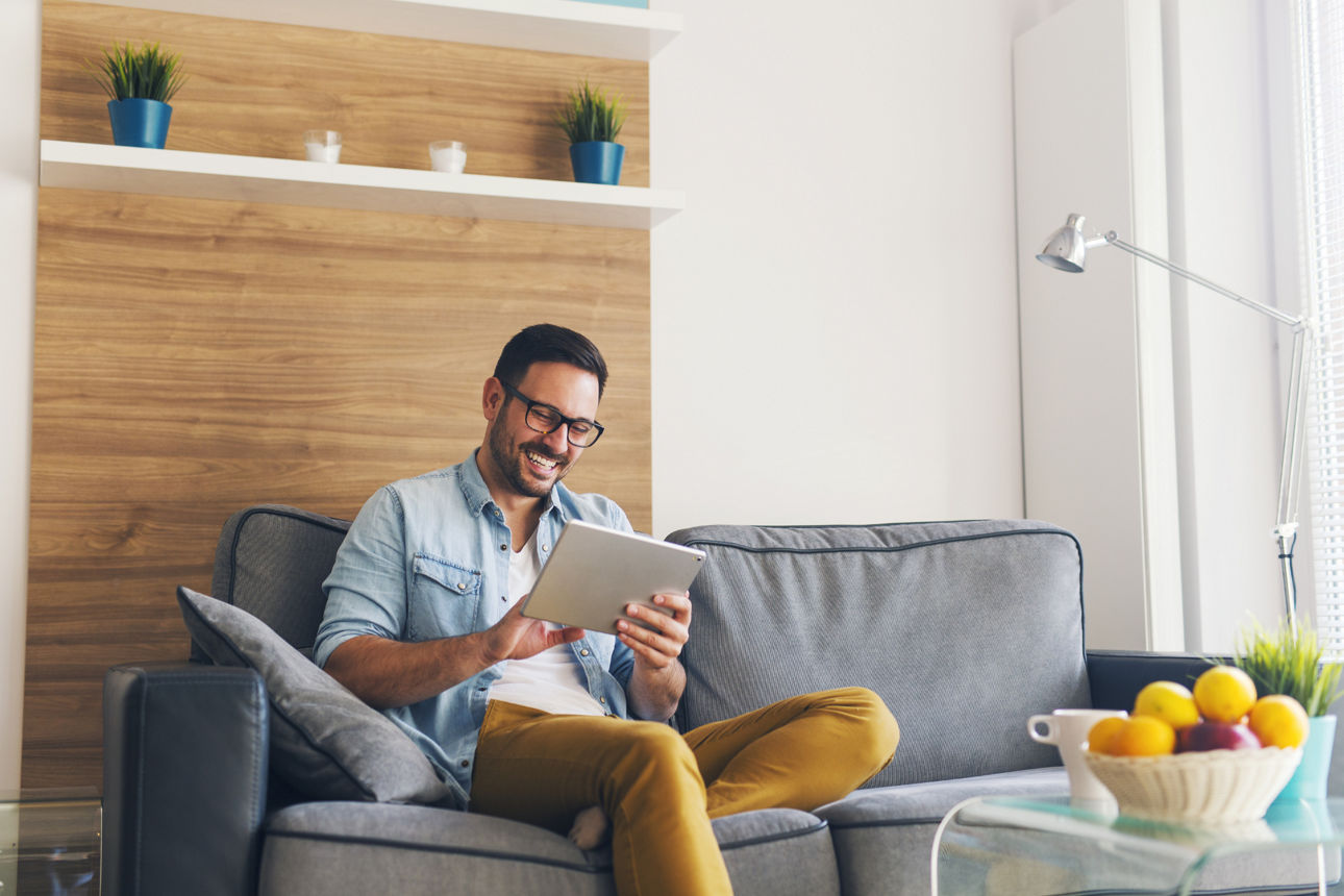 Ein Mann entspannt sitzend auf seiner Couch, hält ein Tablet in der Hand