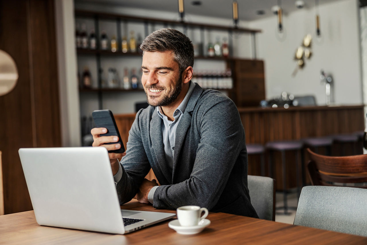 Mann mit Handy sitzt vor einem Laptop