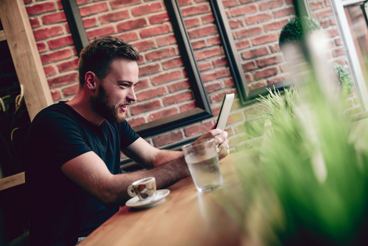 Bild eines Mannes der in einem Cafe an seinem Tablet einen Video-Call führt