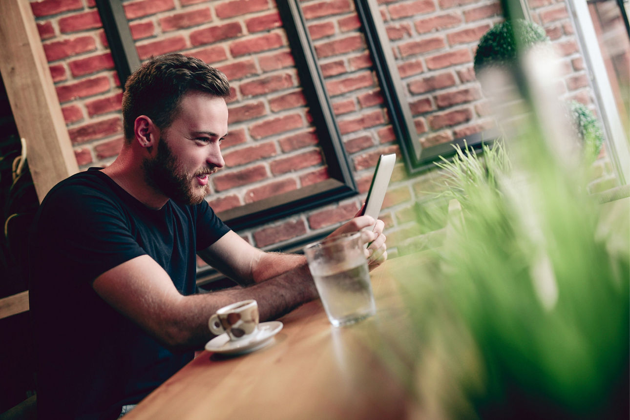 Bild eines Mannes der in einem Cafe an seinem Tablet einen Video-Call führt