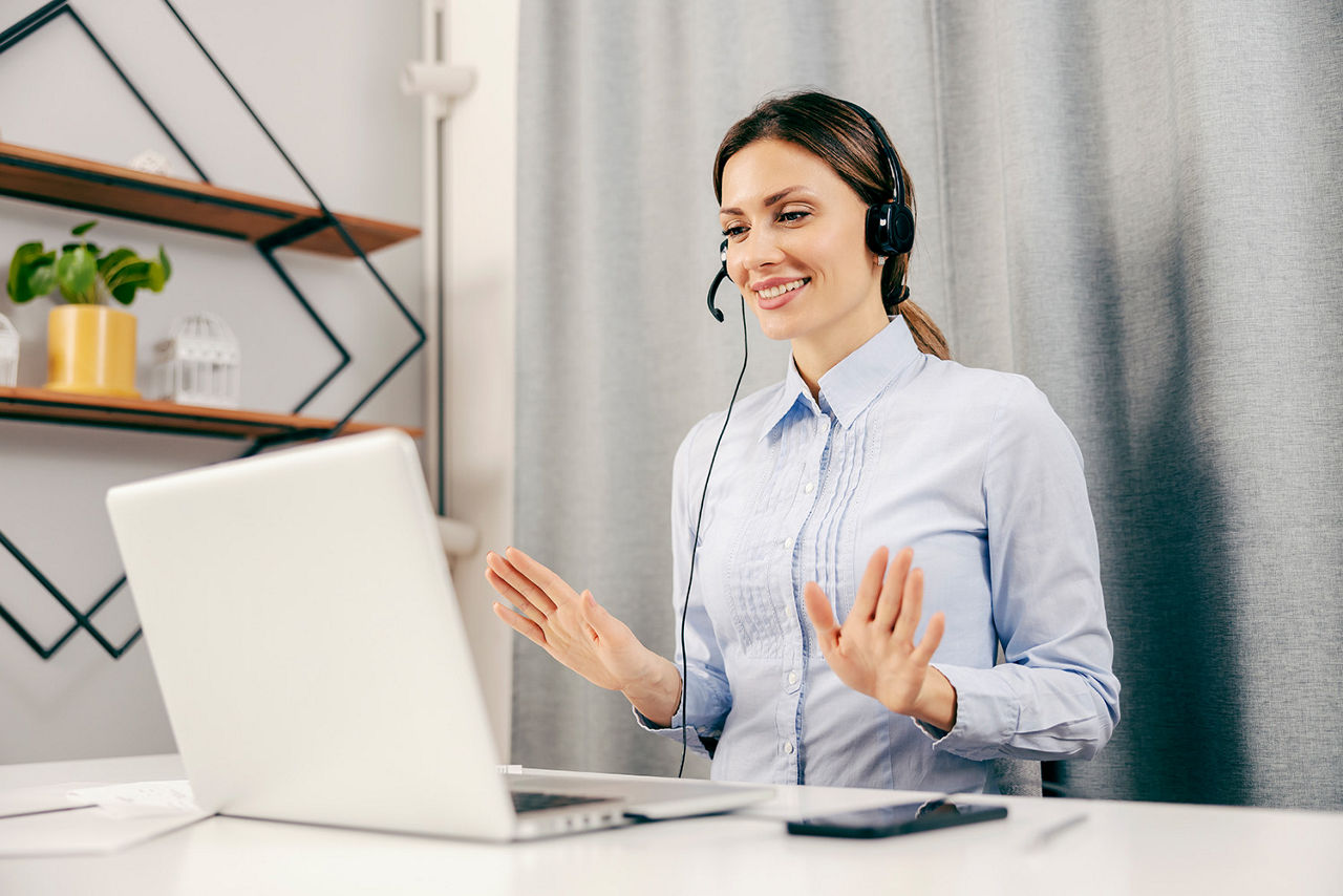 Frau sitzt am Schreibtisch hat ein Headset auf und teloniert online