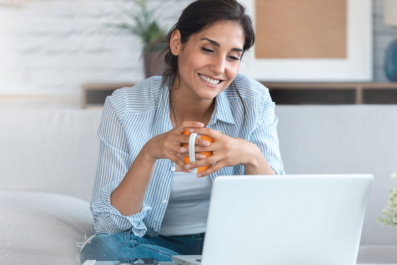 Junge Frau sitzt auf dem Sofa und blickt auf den Bildschirm eines Laptops
