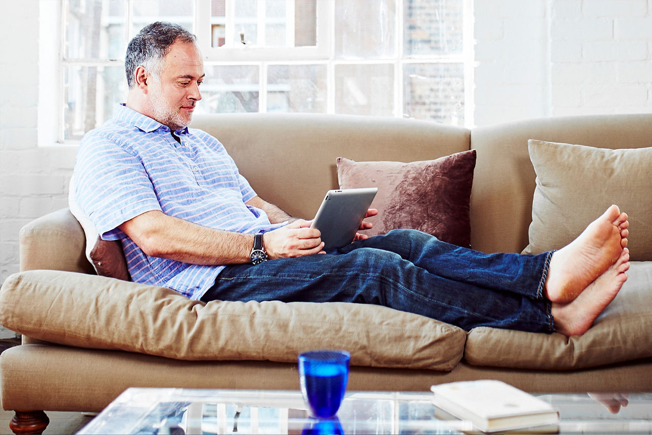 Mann sitzt mit Tablet auf der Couch