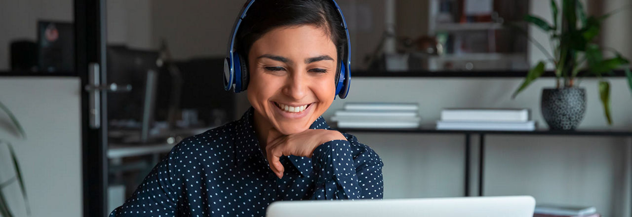 Junge Frau mit Headset lächelt in die Kamera, im Hintergrund ein heller, unscharfer Innenraum.