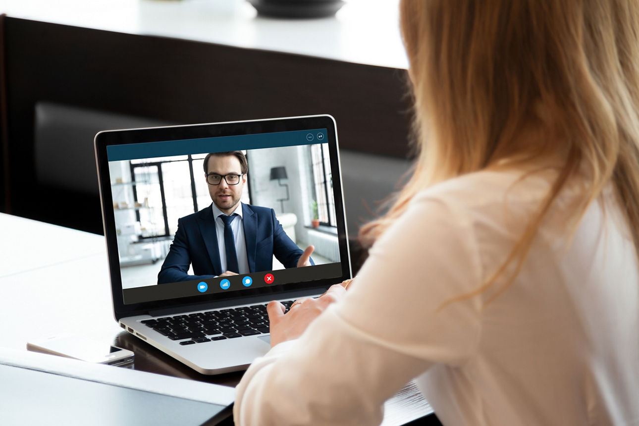 Ein junger Mann in gelbem Pullover sitzt in einer Küche und schaut lächelnd auf sein Smartphone.