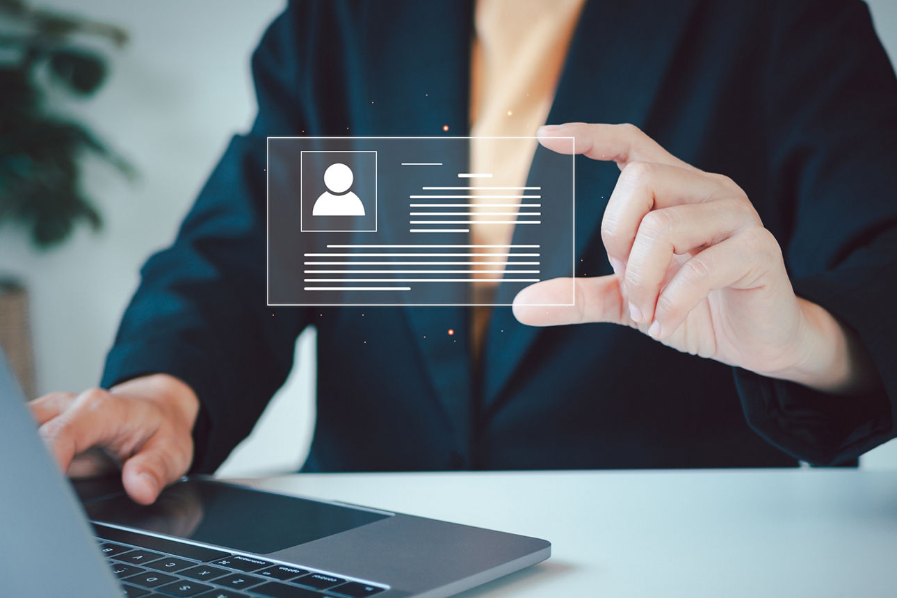 Ausschnitt einer vor einem Laptop sitzenden Person, die einen digitalen Ausweis in der Hand hält.