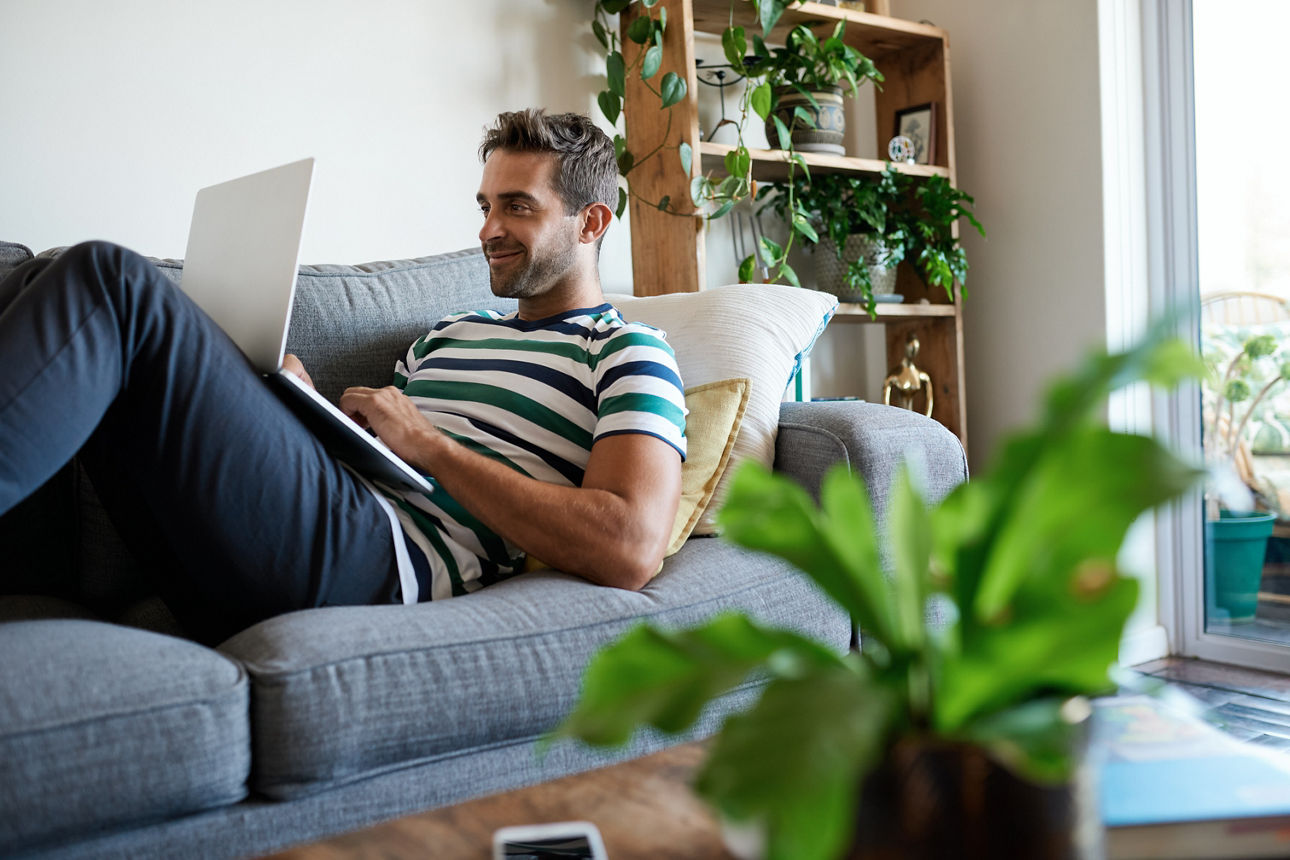 Lächelnder Mann sitzt mit Laptop auf Sofa.