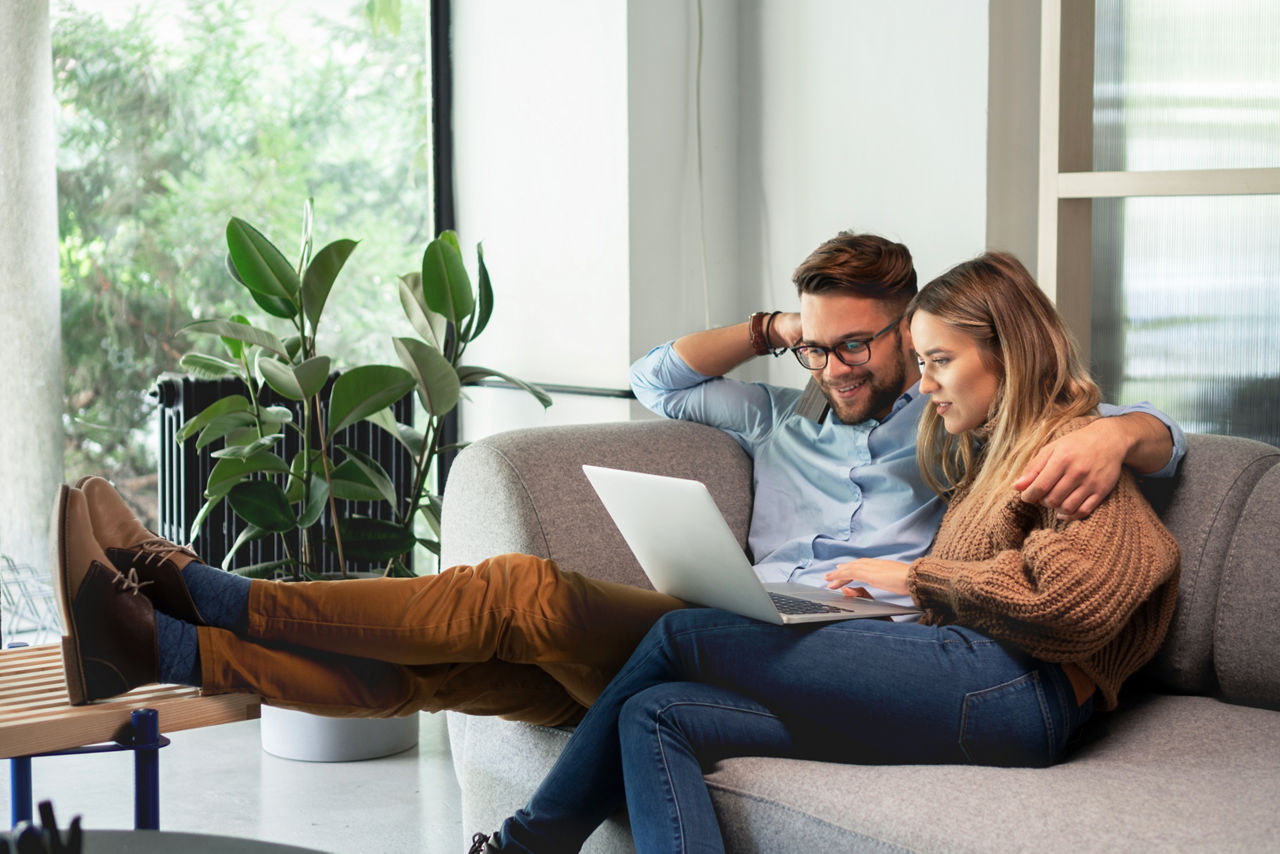 Ein Mann und eine Frau sitzen vor einem Laptop auf der Couch