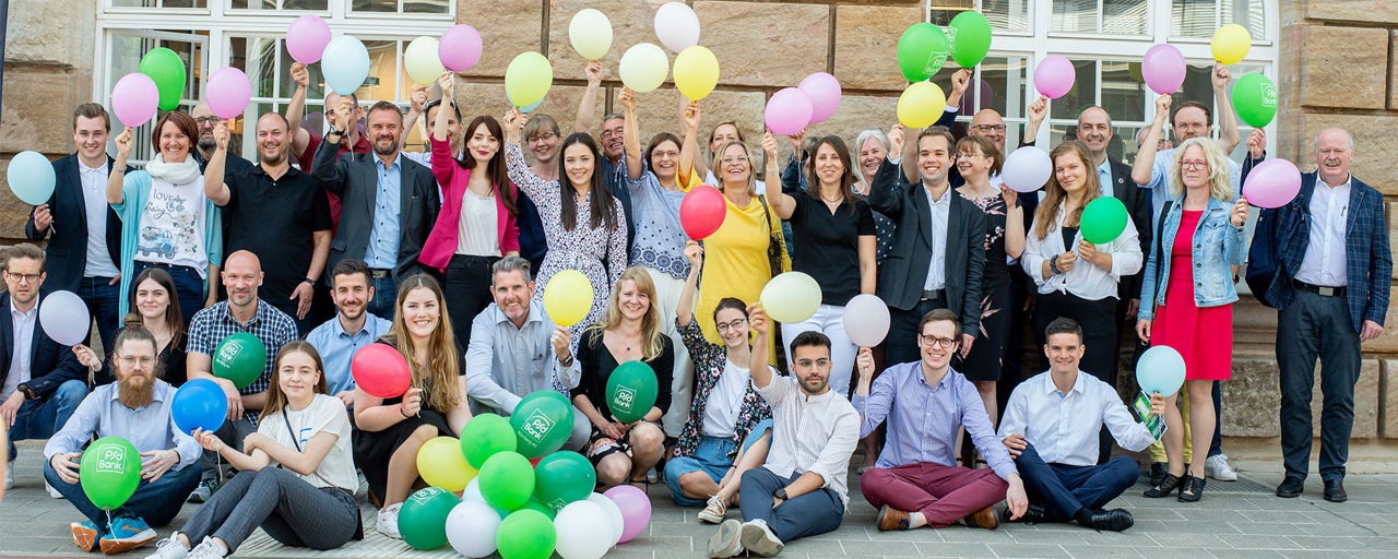 Mitarbeitende der PSD Bank Nürnberg halten Luftballons in viele Farben in die Kamera