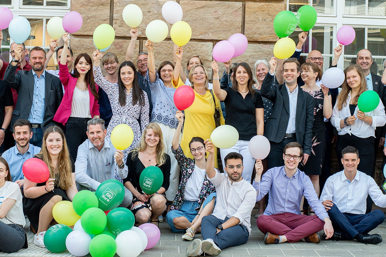 Mitarbeitende der PSD Bank Nürnberg halten Luftballons in viele Farben in die Kamera