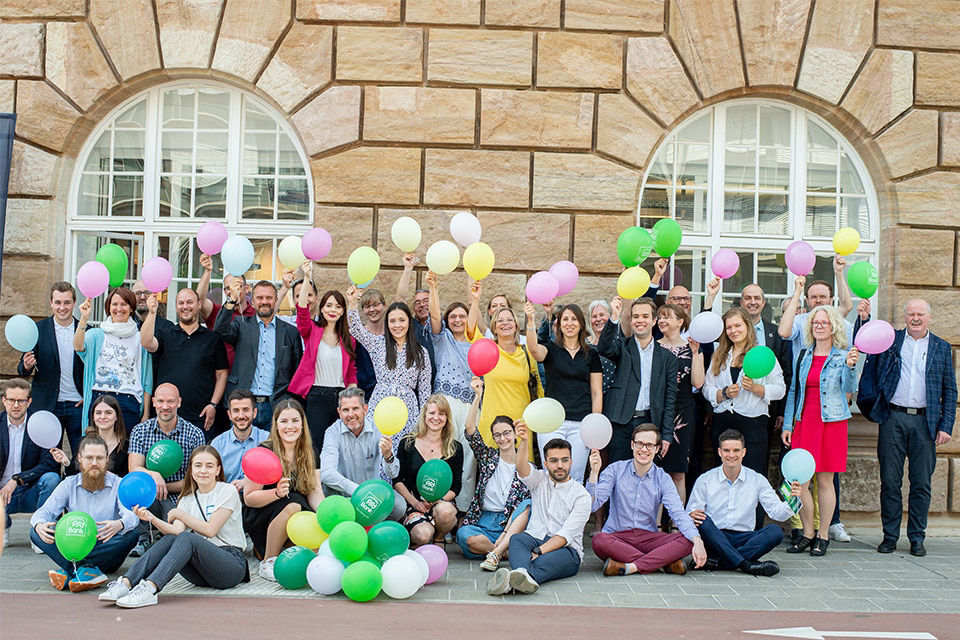Mitarbeitende der PSD Bank Nürnberg halten Luftballons in viele Farben in die Kamera Mitarbeitende der PSD Bank Nürnberg halten Luftballons in viele Farben in die Kamera