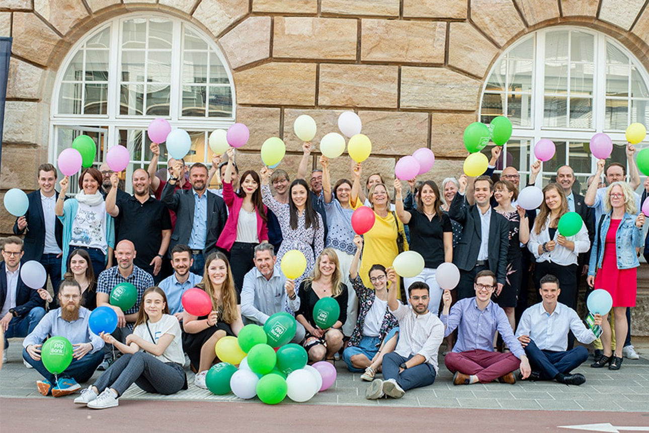Mitarbeitende der PSD Bank Nürnberg halten Luftballons in viele Farben in die Kamera