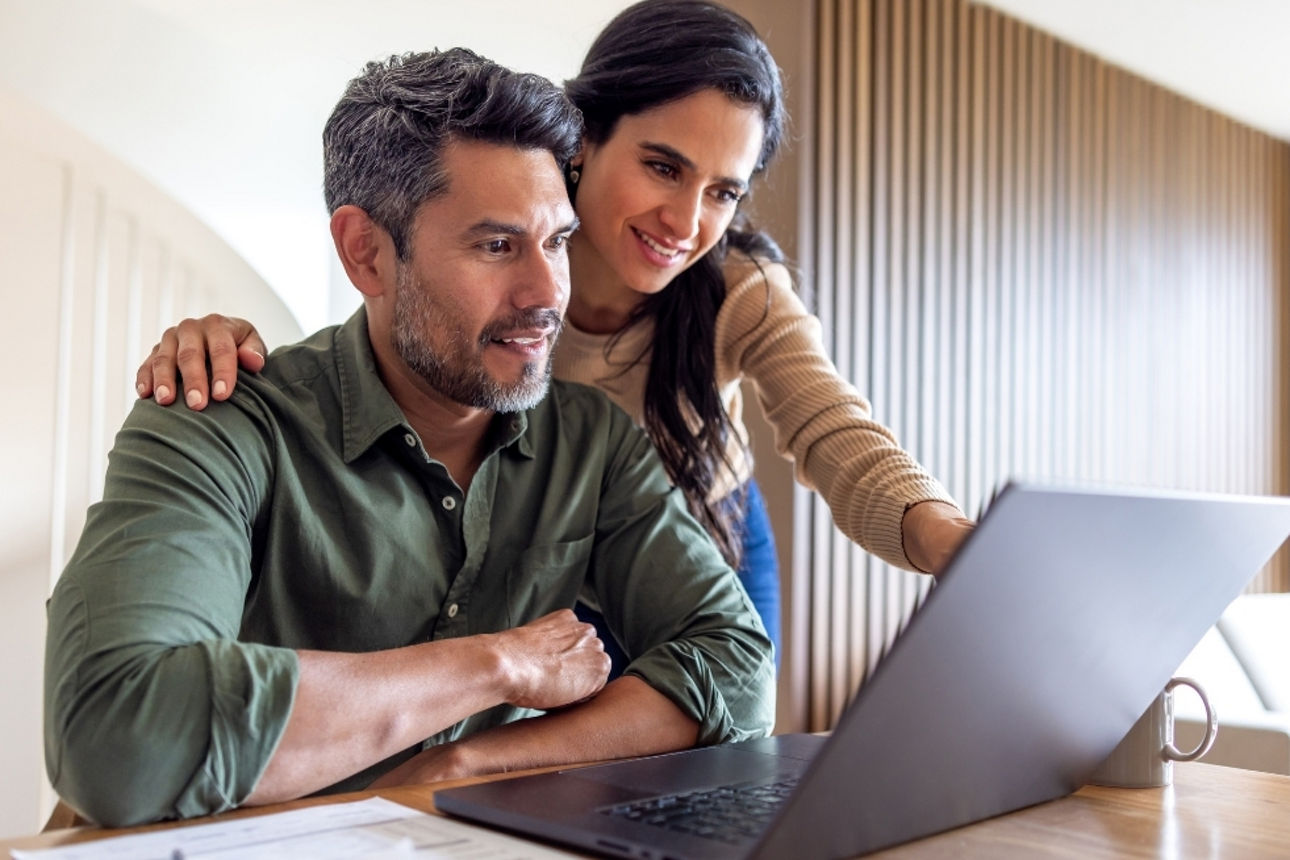 Pärchen sitzt vor Laptop, Frau zeigt auf Bildschirm