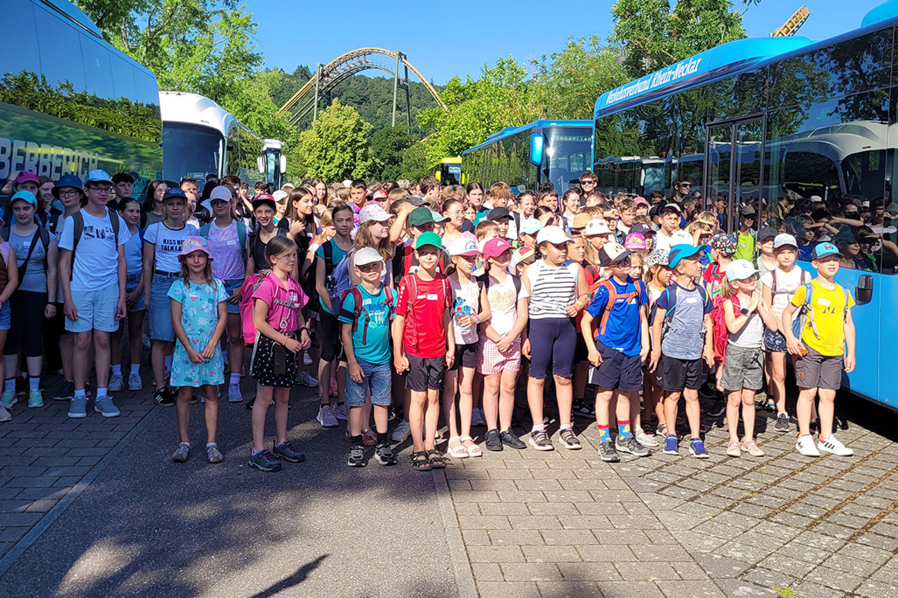 Eine große Gruppe Kinder steht zwischen mehreren Bussen