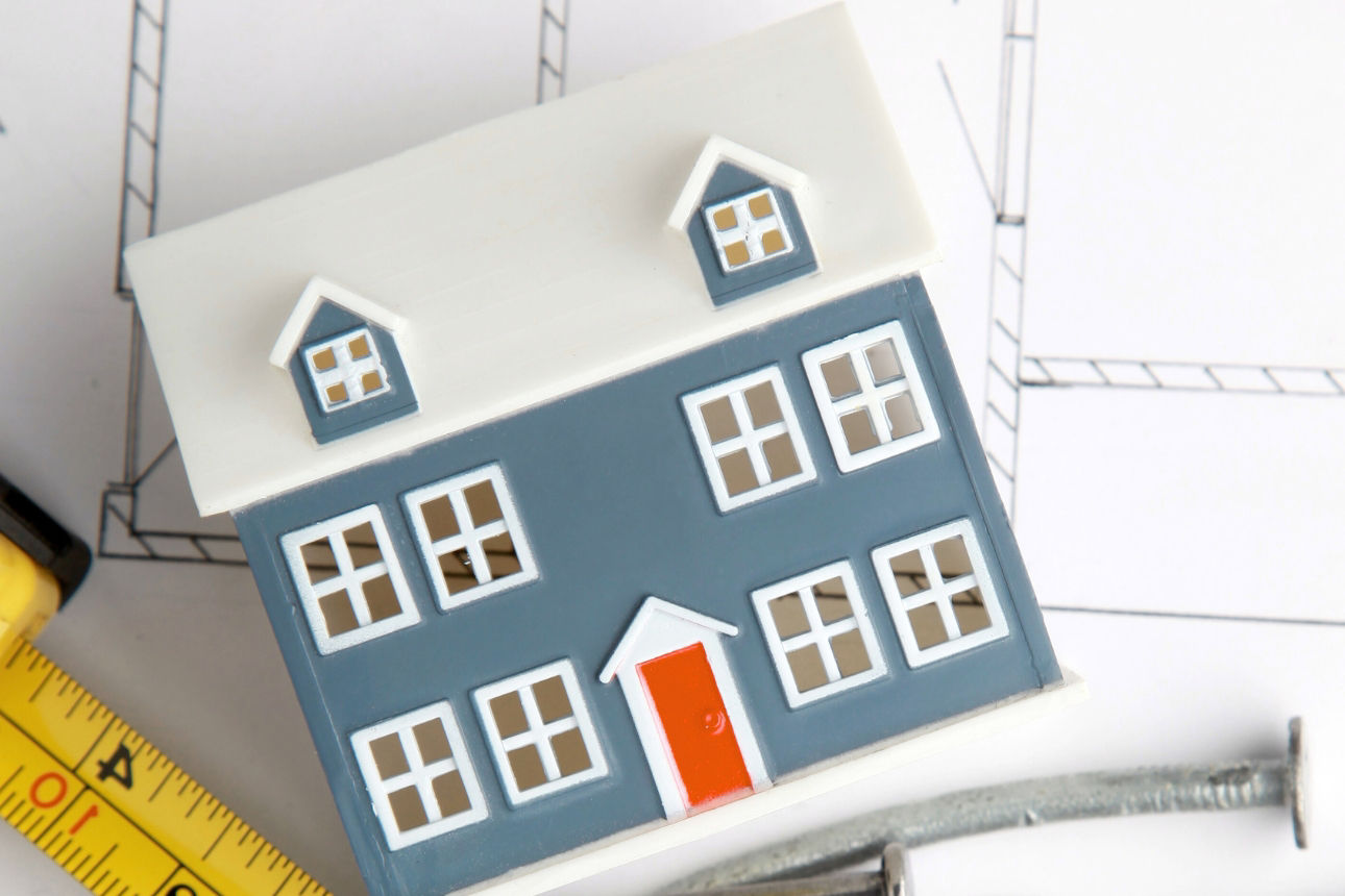 Bauplan mit Hausmodell und Maßband