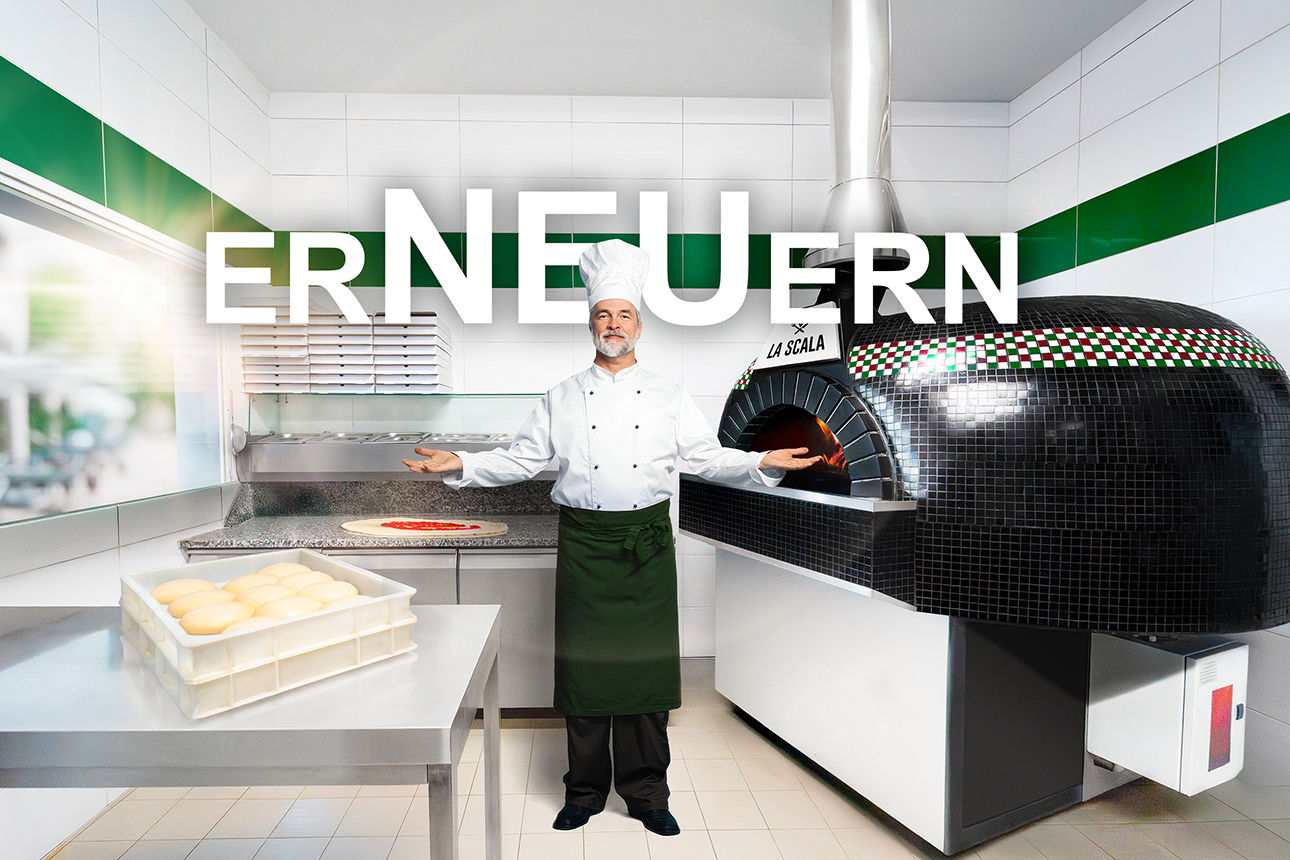 Ein Koch posiert mit offenen Armen in einer Großküche