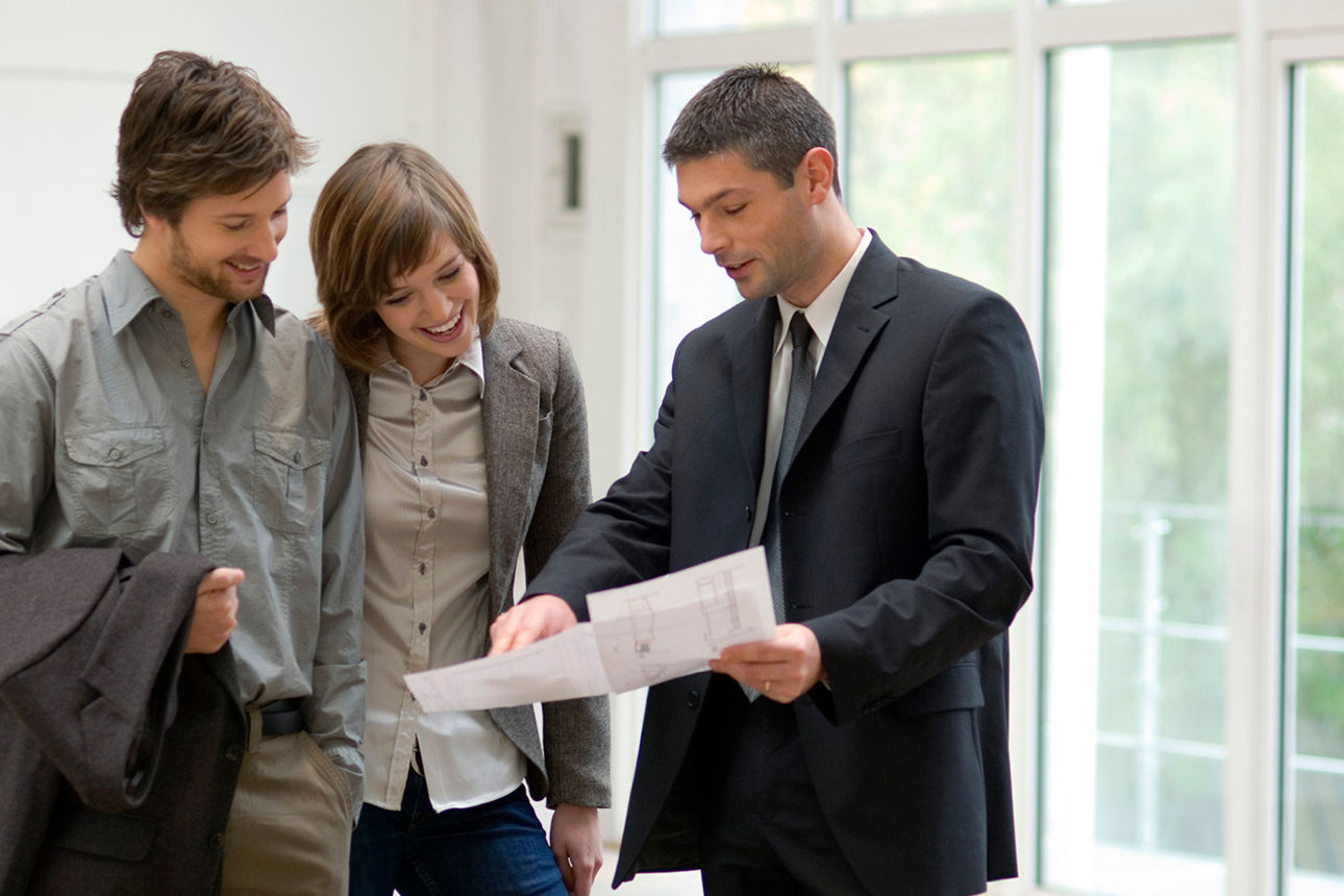Lächelnde Bankberaterin im Gespräch mit einem Ehepaar im Rohbau