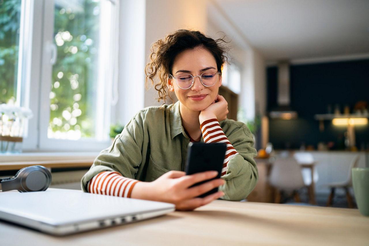 Junge Frau sitzt am Tisch mit Smartphone in der Hand