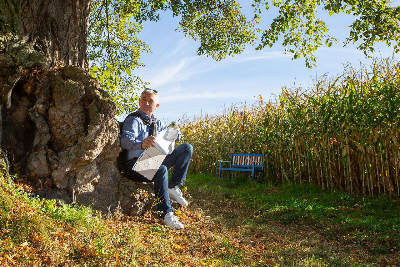 Mann sitzt mit Papier in den Händen an einem Baum