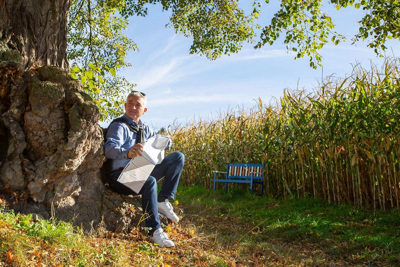 Mann sitzt mit Papier in den Händen an einem Baum